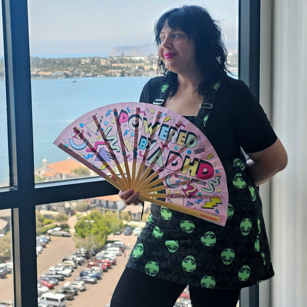 Powered by ADHD bamboo clack fan by Harlem Starlet, a bold neurodivergent statement hand fan perfect for Pride festivals, raves, queer events and ADHD babes who love funny statement fans.